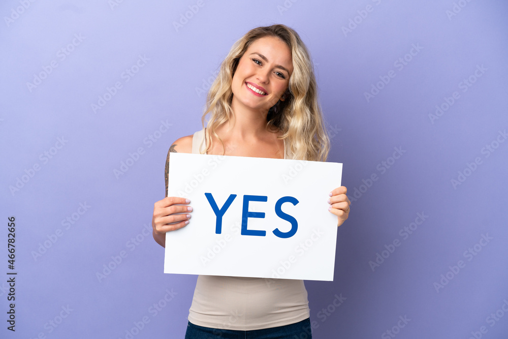 Young Brazilian woman isolated on purple background holding a placard with text YES with happy expression Young Brazilian woman isolated on purple background holding a placard with text YES with happy expression