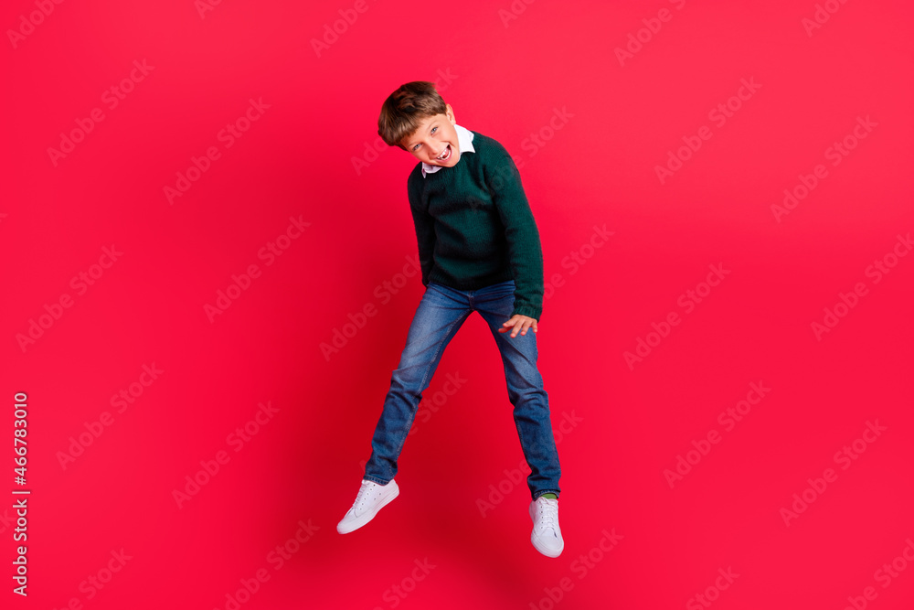 Photo of cute charming school boy wear knitted pullover smiling jumping high isolated red color background