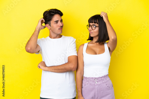 Young mixed race couple isolated on yellow background having doubts while scratching head © luismolinero