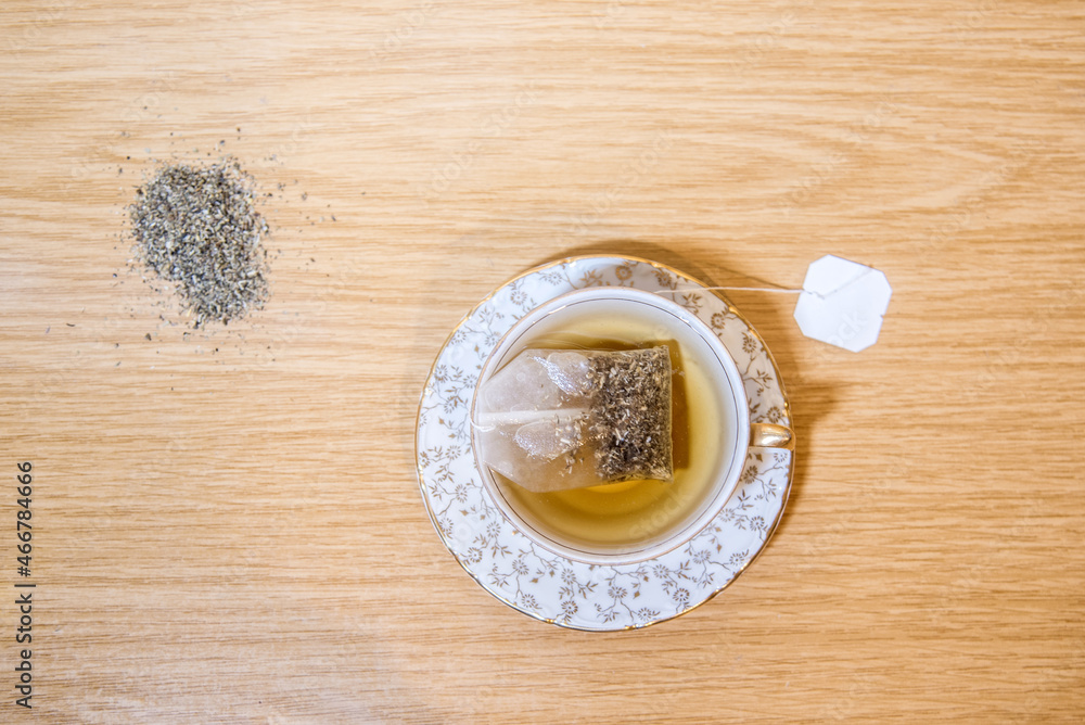 Vista cenital de una taza de té con una bolsita de té de manzanilla en el interior. Hierbas secas en la mesa. Adornos florales dorados. Fondo de madera Vista cenital de una taza de té con una bolsita de té de manzanilla en el interior. Hierbas secas en la mesa. Adornos florales dorados. Fondo de madera