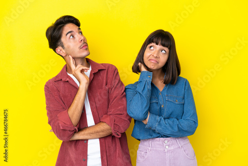 Young mixed race couple isolated on yellow background thinking an idea while scratching head