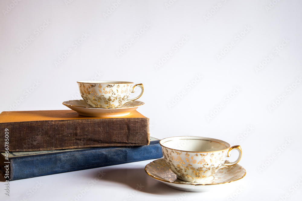 Libros y dos tazas de té pequeñas con adornos de flores doradas pintadas a mano sobre un fondo blanco. Concepto de lectura mientras bebe una bebida herbal tibia y saludable Libros y dos tazas de té pequeñas con adornos de flores doradas pintadas a mano sobre un fondo blanco. Concepto de lectura mientras bebe una bebida herbal tibia y saludable