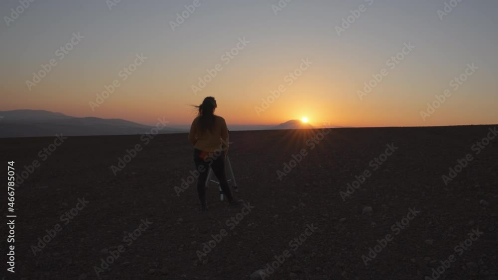 Wide angle view of a woman filming a sunset with a camera and a tripod in the desert. Slow motion. Wide angle view of a woman filming a sunset with a camera and a tripod in the desert. Slow motion.