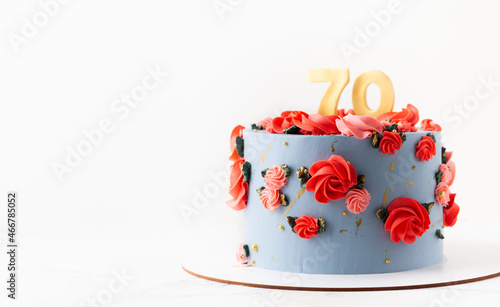 Birthday cake with blue cream cheese frosting decorated with red flowers on the white background. Happy 70 years anniversary