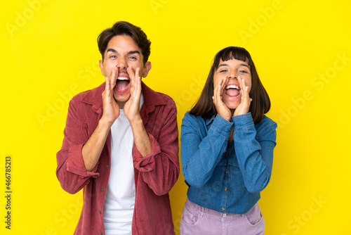 Young mixed race couple isolated on yellow background shouting and announcing something