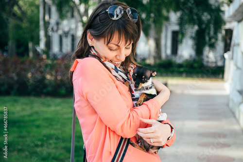 Happy young caucasian woman hugging her small dog  Russian Toy or Russian Toy Terrier  dressed in autumn suit. Love pets concept