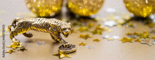 Banner bronze figure of a tiger with a coin - the symbol of the Chinese new year 2022 on a background of stars, golden shiny balls, copy space. Wishes of good luck, financial well-being and wealth