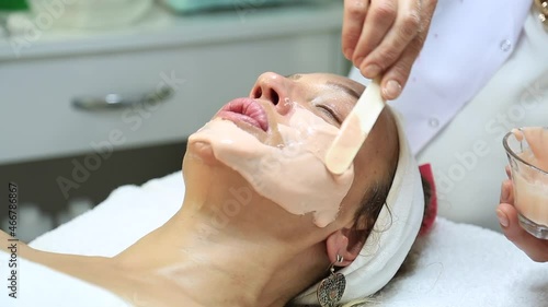 Facial peeling mask, spa beauty treatment, skin care. Woman getting facial treatment by beauty at spa salon, side view close up. Beautiful woman getting face massage in beauty spa