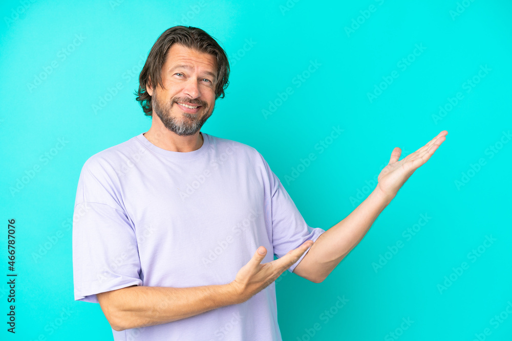 Senior dutch man isolated on blue background extending hands to the side for inviting to come Senior dutch man isolated on blue background extending hands to the side for inviting to come