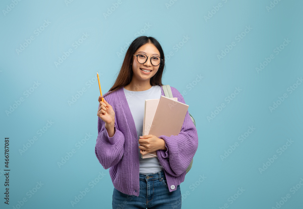 I know the answer. Excited asian female student in eyeglasses holding notepad and pointing pencil up, blue background I know the answer. Excited asian female student in eyeglasses holding notepad and pointing pencil up, blue background