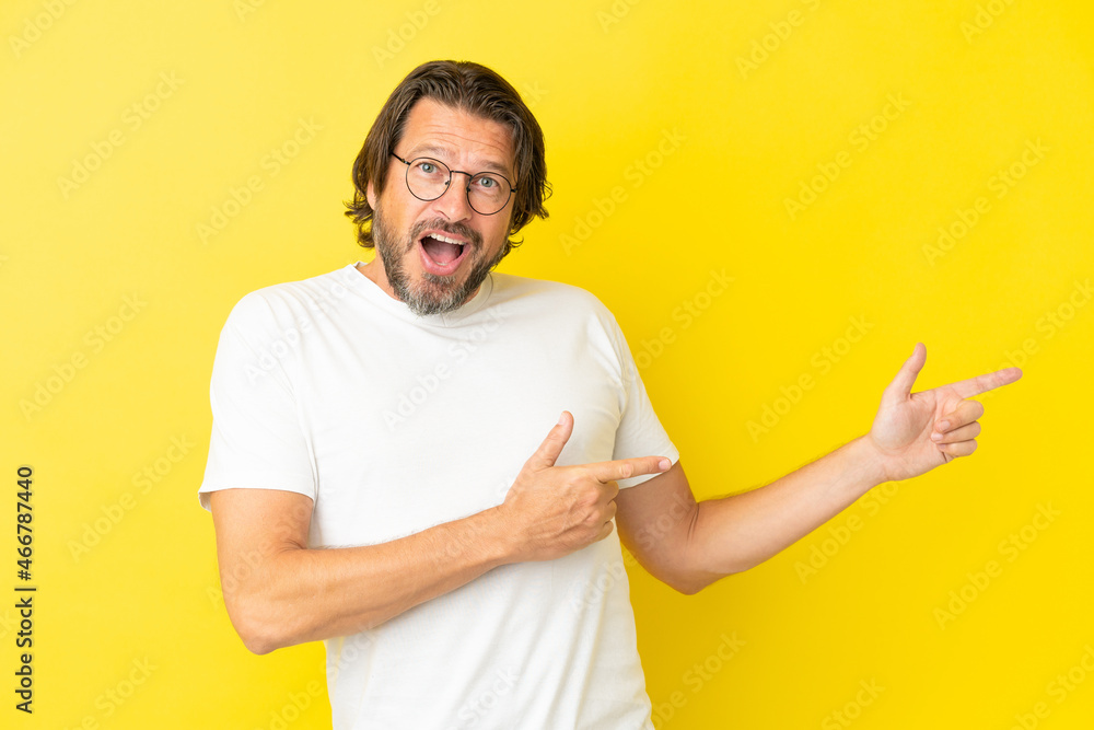 Senior dutch man isolated on yellow background surprised and pointing side Senior dutch man isolated on yellow background surprised and pointing side