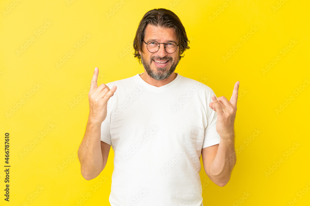 Senior dutch man isolated on yellow background making horn gesture Senior dutch man isolated on yellow background making horn gesture