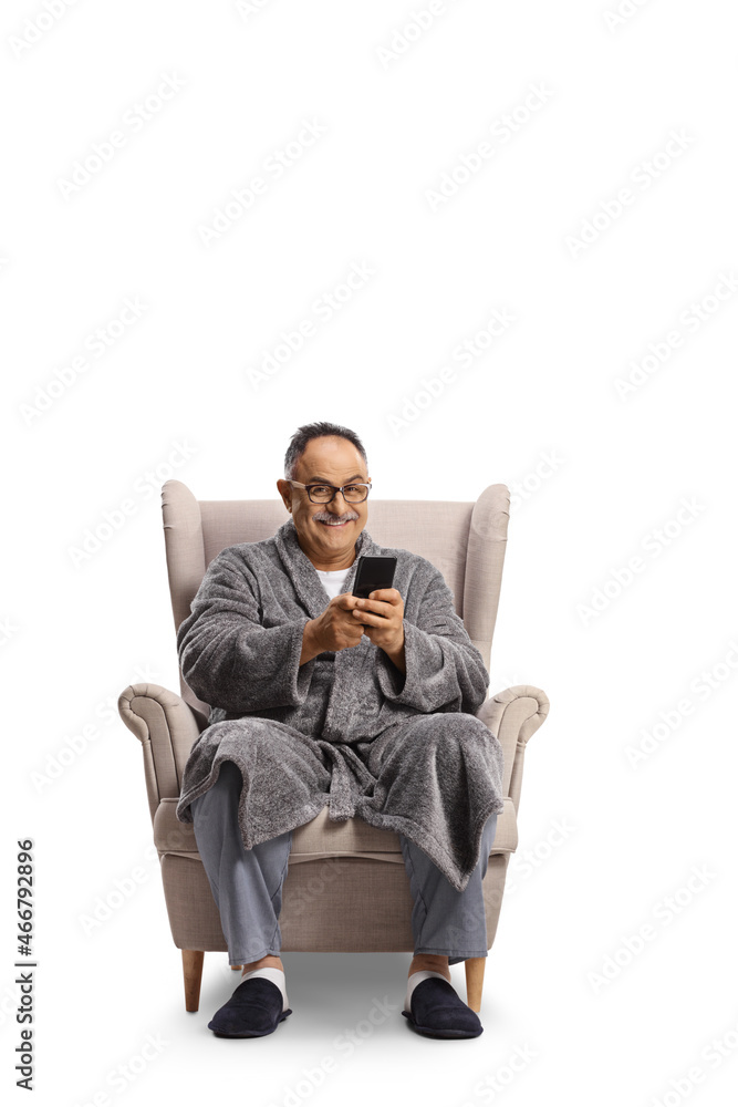 Mature man in a bathrobe sitting in an armchair and using a smartphone Mature man in a bathrobe sitting in an armchair and using a smartphone