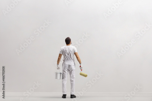 Fototapeta Naklejka Na Ścianę i Meble -  Rear view shot of a painter in front of a wall holding a bucket ana a paint roller