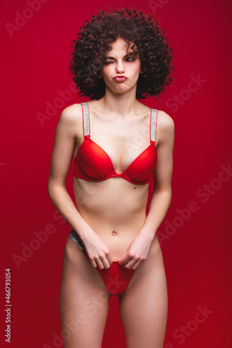 Funny portrait of an attractive girl with African curls. Sexy girl in a red bikini on a red background.