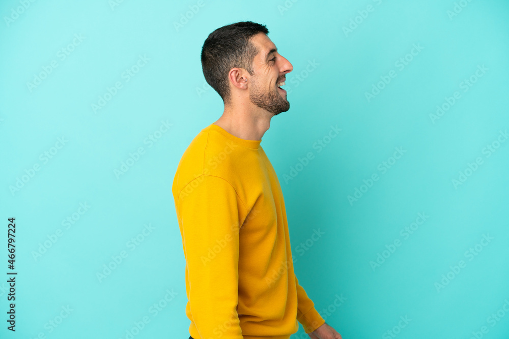 Young handsome caucasian man isolated on blue background laughing in lateral position Young handsome caucasian man isolated on blue background laughing in lateral position