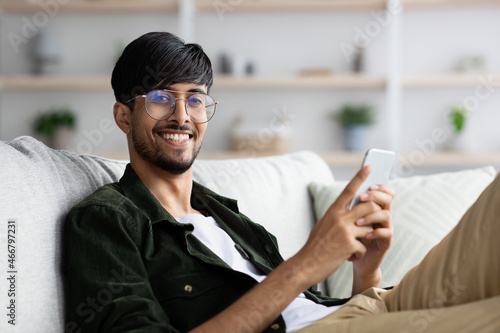 Positive arabic guy playing mobile games at home © Prostock-studio