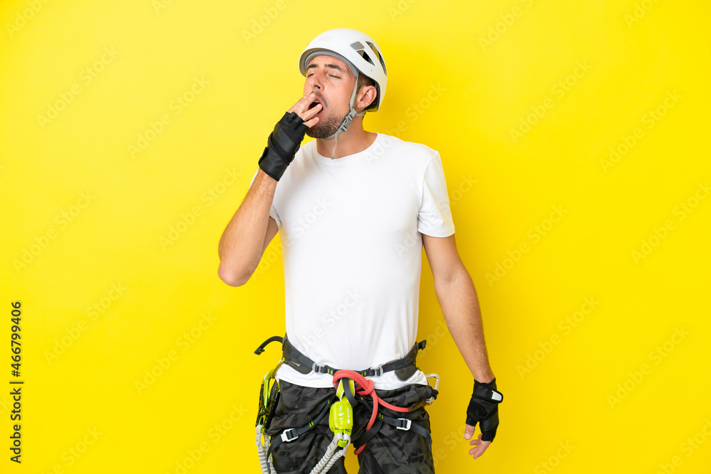 Young rock- climber man isolated on yellow background yawning and covering wide open mouth with hand