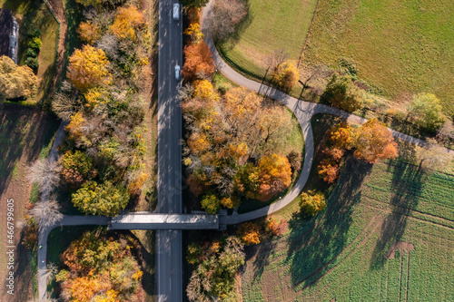 Top down view at a autumnal landscape with a rural street and a covered bridge for pedestians straight from above in Oberhaching.