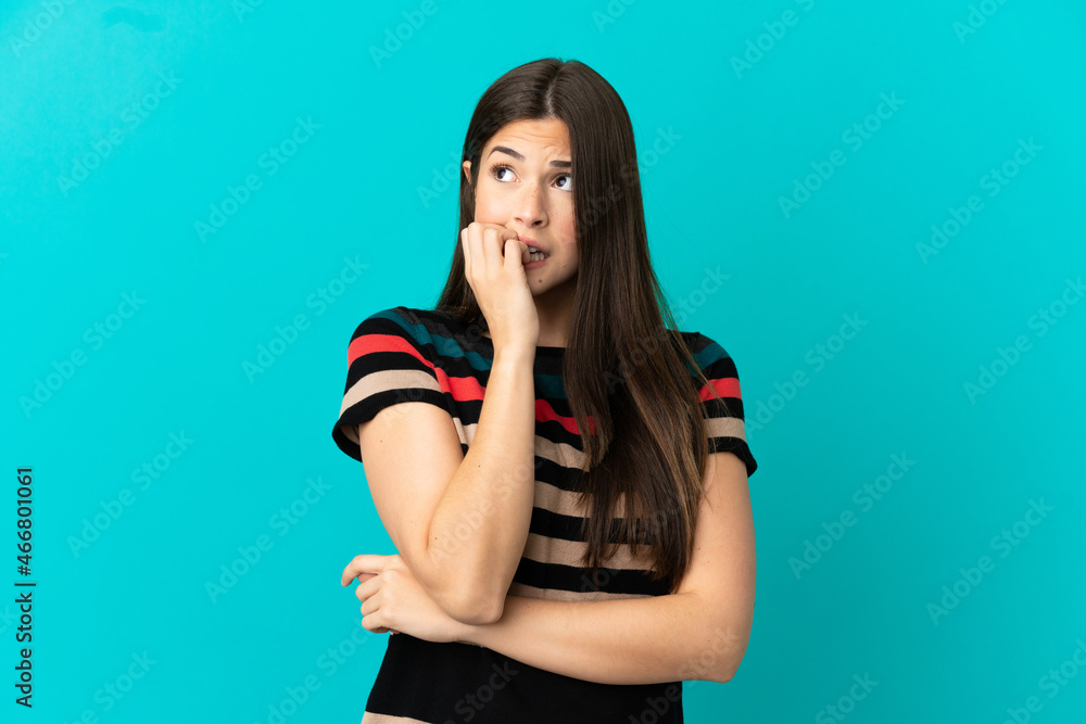 Teenager Brazilian girl over isolated blue background is a little bit nervous Teenager Brazilian girl over isolated blue background is a little bit nervous