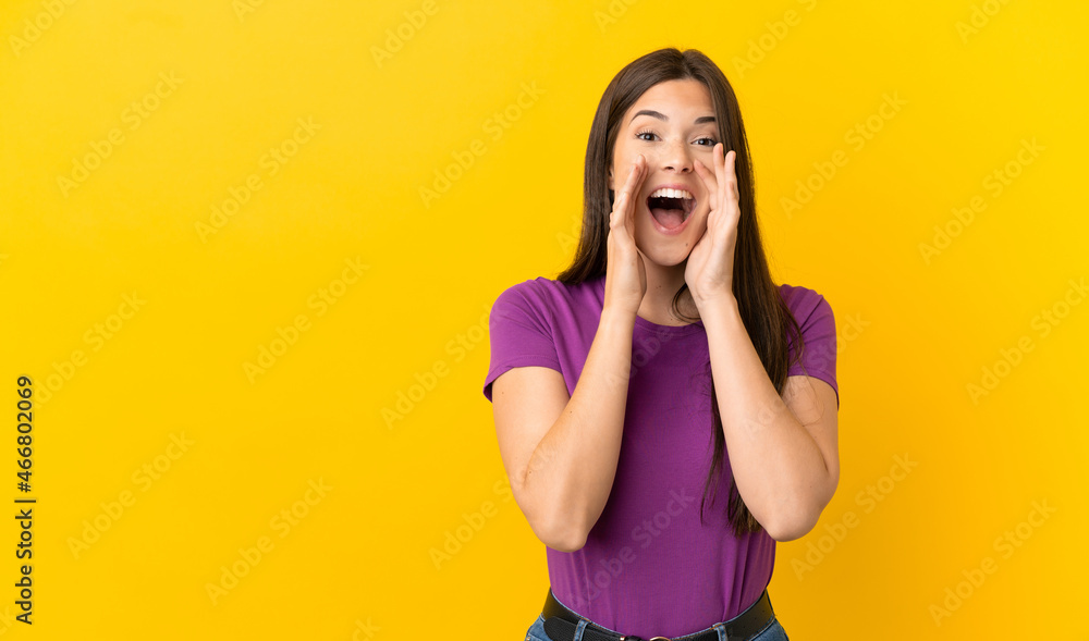 Teenager Brazilian girl over isolated yellow background shouting and announcing something Teenager Brazilian girl over isolated yellow background shouting and announcing something