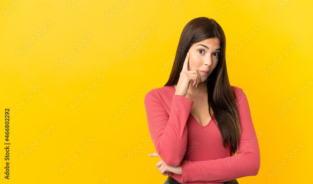 Teenager Brazilian girl over isolated yellow background thinking an idea Teenager Brazilian girl over isolated yellow background thinking an idea