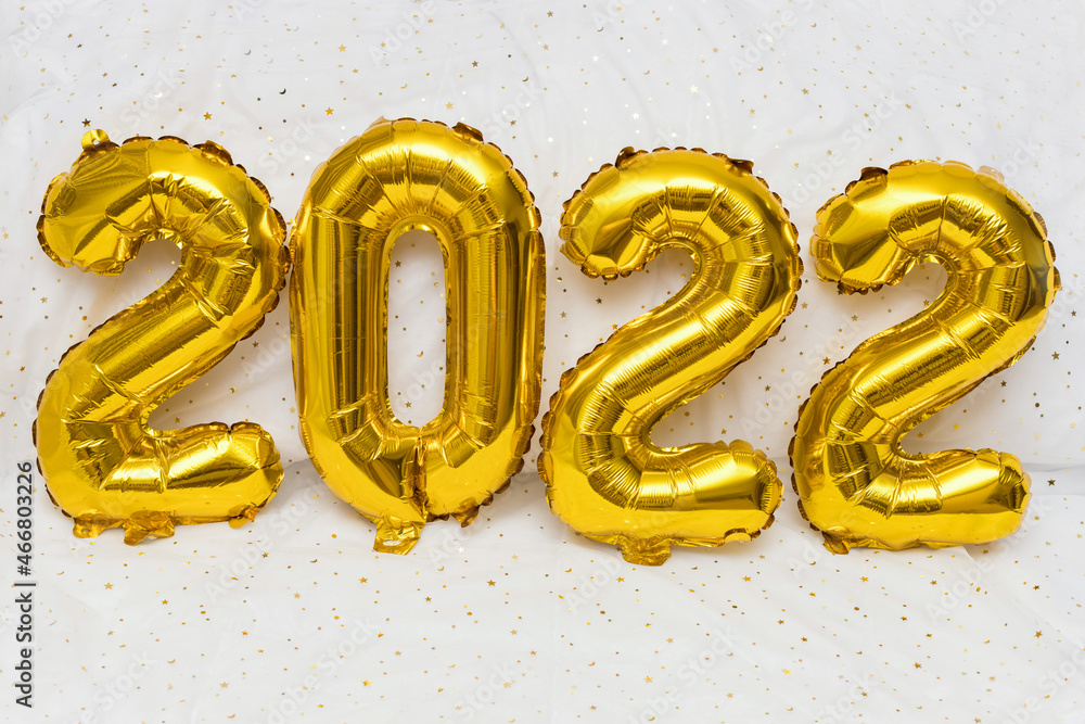Happy New Year 2022. Golden inflatable figures on a white background with stars in close-up. the concept of a postcard. Happy New Year 2022. Golden inflatable figures on a white background with stars in close-up. the concept of a postcard.