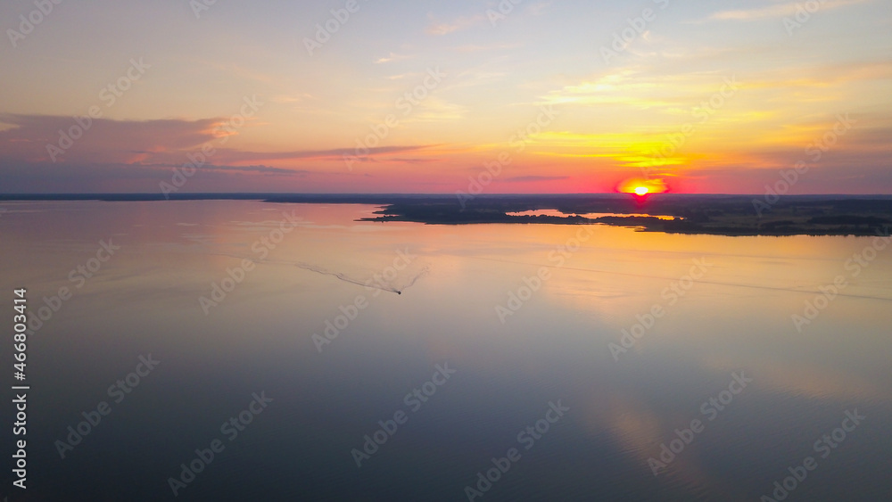 Beautiful sunset over the lake. Clouds on orange sky during summer sundown. Bird's eye view of the lake and forest.