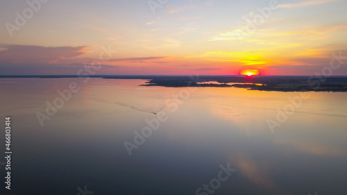 Beautiful sunset over the lake. Clouds on orange sky during summer sundown. Bird's eye view of the lake and forest.
