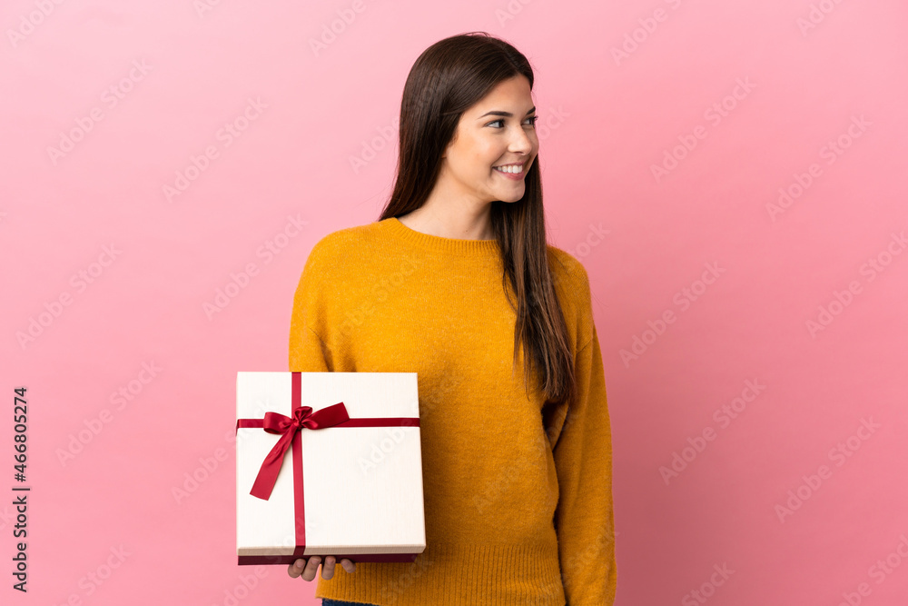 Teenager Brazilian girl holding a gift over isolated pink background looking side Teenager Brazilian girl holding a gift over isolated pink background looking side