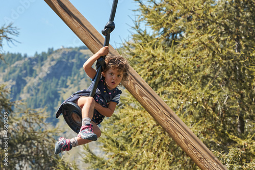 Happy funny curly-haired little girl riding on a high swing in the mountains. A surprised expression. Light curly hair. He looks at the camera.