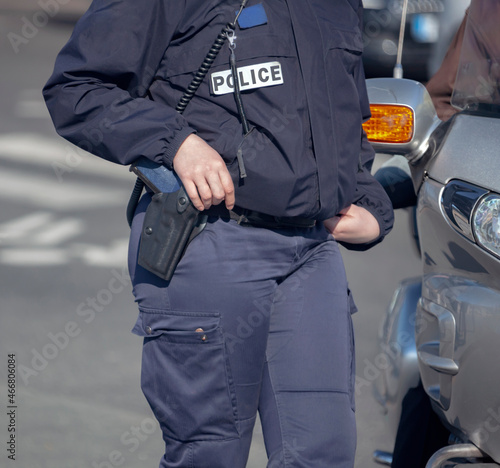 Woman in police uniform with weapons and communications equipment at car on the road.