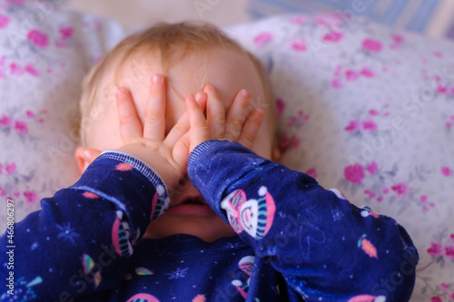 adorable little blonde girl playing peekaboo, little girl cover her own eyes with her hands, selective focus