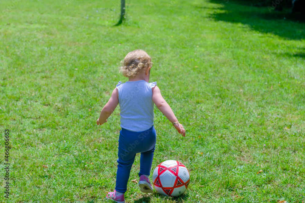 Blonde little girl playing football and try to catch the ball in the garden, child activity concept idea Blonde little girl playing football and try to catch the ball in the garden, child activity concept idea