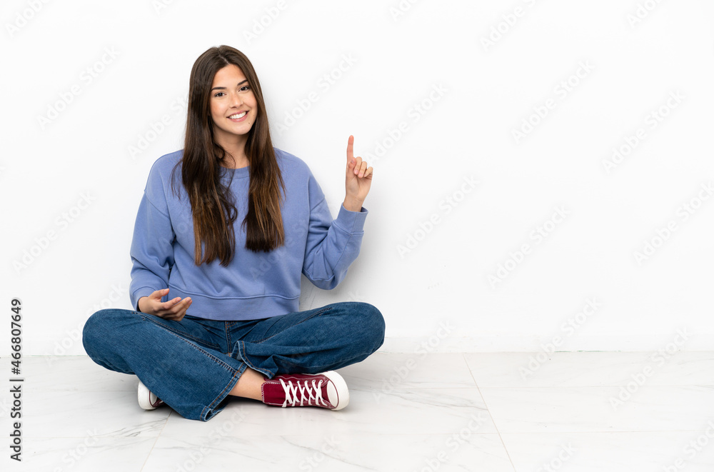 Young woman sitting on the floor showing and lifting a finger in sign of the best Young woman sitting on the floor showing and lifting a finger in sign of the best