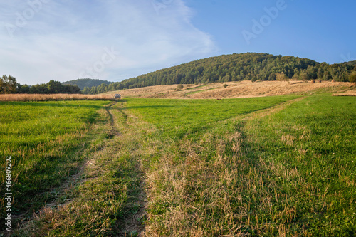 A country road leads through a wheat field in the mountains, an old car is far on the horizon. Gorgeous landscape, beauty of nature, outdoor