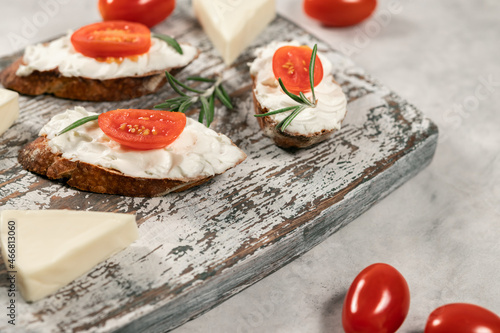 Bread with cream cheese and tomatoes, sandwiches on the wooden board on grey background