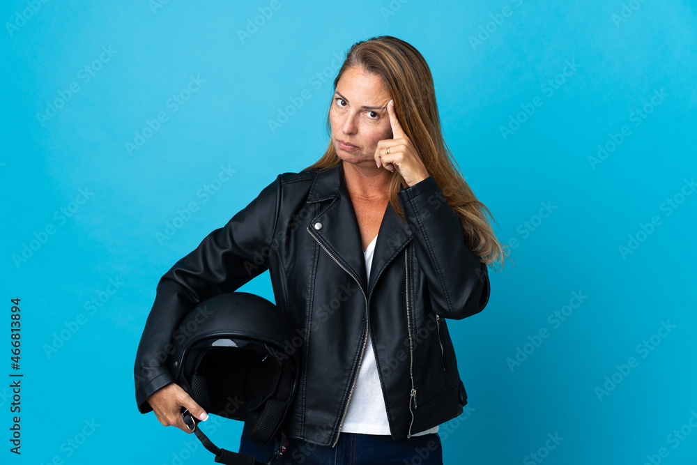 Middle age woman holding a motorcycle helmet isolated on blue background thinking an idea Middle age woman holding a motorcycle helmet isolated on blue background thinking an idea