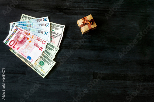 lot of euro, US dollars bills banknotes with gift box with golden ring jewelry on black wooden table. buying surprise, present for marrige, money cash finance budget concept, top view, copy space