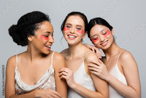 Happy multiethnic women with eye patches hugging isolated on grey