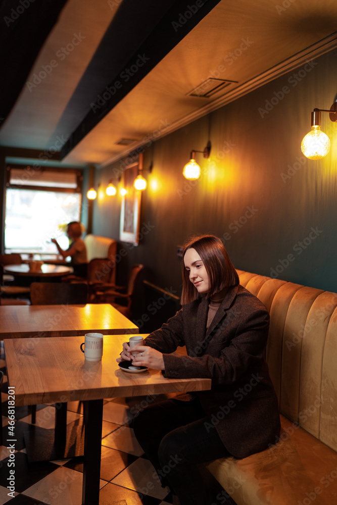 Drinking coffee. Pretty young woman holding cup of beverage while sitting at cafe. Drinking coffee. Pretty young woman holding cup of beverage while sitting at cafe.