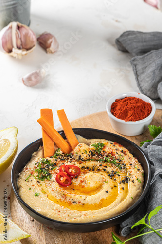 Delicious hummus in ceramic bow lwith  carrot stick dipped in hummus. Colorful snack composition on a white background. photo