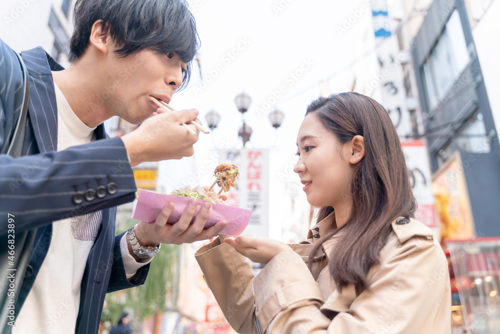 Fototapeta premium 大阪を観光するカップル 道頓堀 たこ焼きを食べる