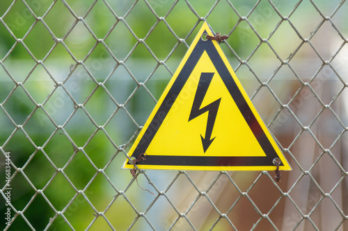 Electrical voltage sign, caution - danger of electric shock, against the background of the melal mesh