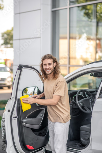 Smiling guy wiping front door of car