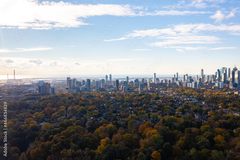 downtown Toronto with Riverdale east park trees with fall colours red green orange and yellow leaf colours. the CN Tower and the Toronto skyline with blue skies and little clouds.