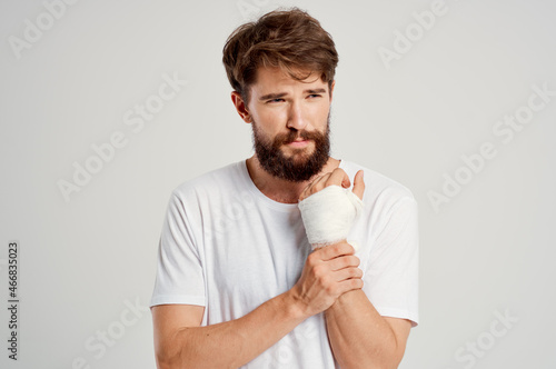 bearded man in a white T-shirt with a bandaged hand posing hospital medicine