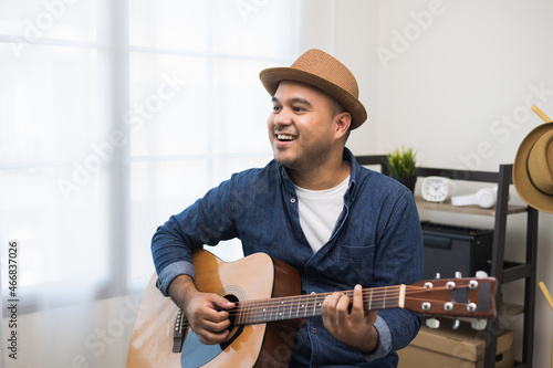 Lifestyle concept. Young asian musician playing guitar in living room at home on this weekend. Relaxing with song and music. Asian man having fun playing acoustic guitar