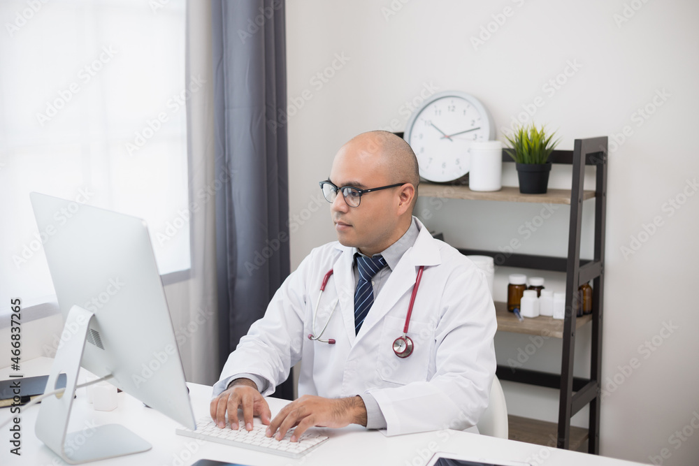 Young asian doctor working online texting on the keyboard video conference with team. Close Up Physician in white coat, stethoscope working with computer