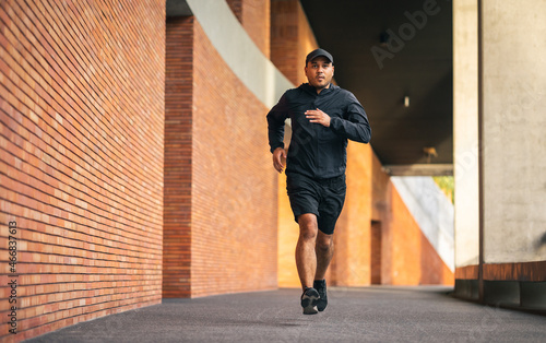 Asia man wearing jacket sportswear running on the road under the building. Young man jogging for exercise in the city. healthy lifestyle and sports concept